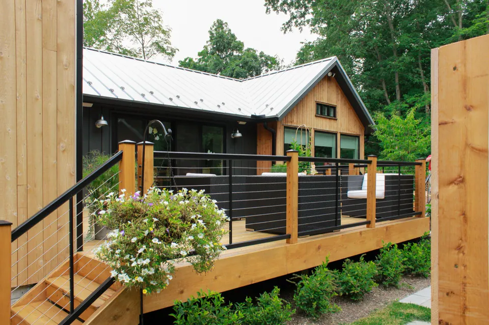 Raised deck with black railings, hanging planter, wood posts, house, and wooded backyard.